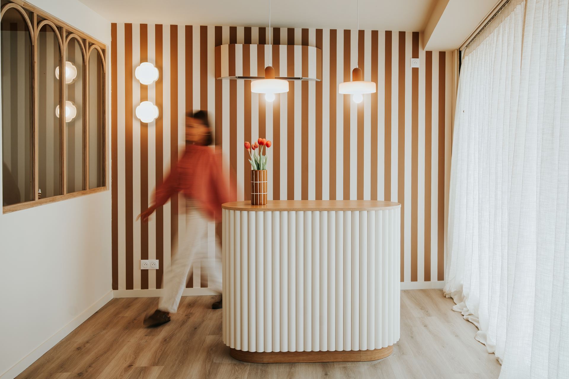 L'accueil de PAUSE studio : comptoir cannelé en bois clair, mur à rayures camel et silhouette floue en mouvement