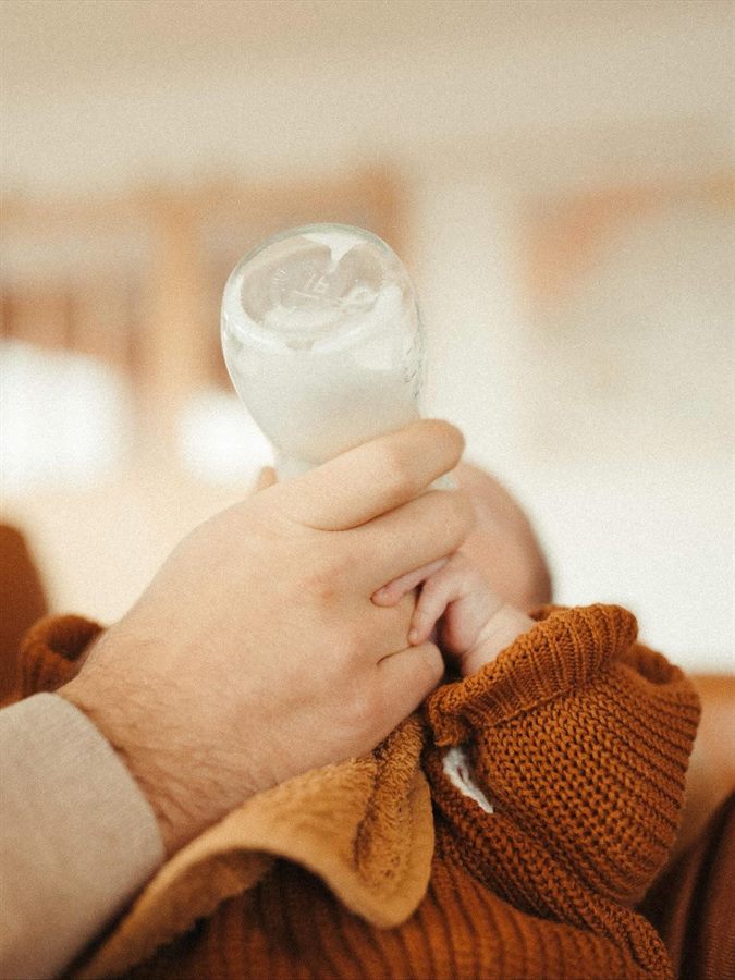 Un nouveau-né tient son biberon, blotti contre un adulte