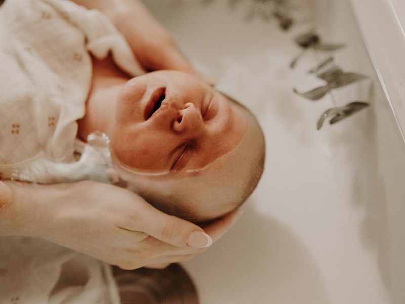 Un nouveau-né détendu dans un bain, soutenu par les mains de la praticienne