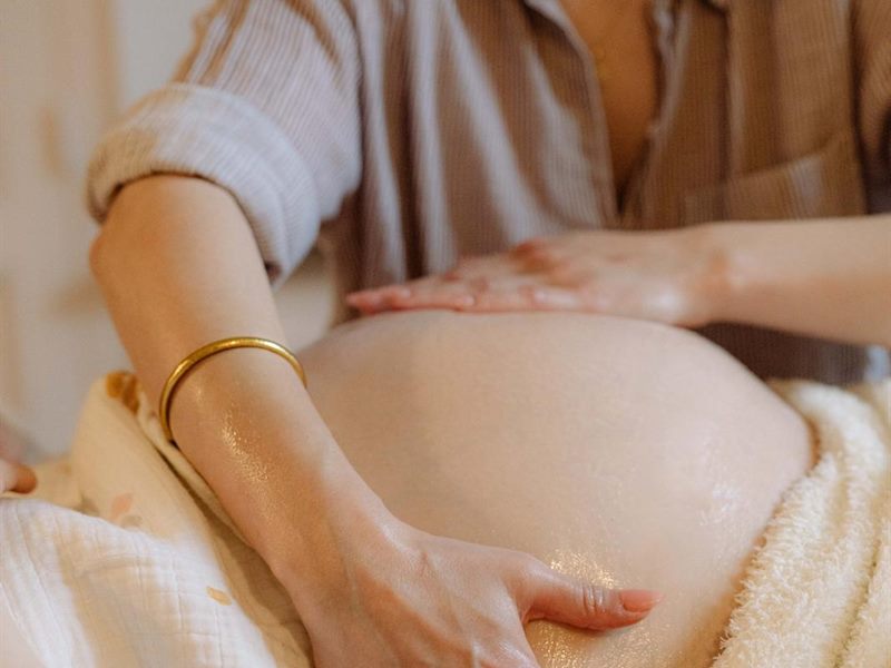 Les mains de la praticienne massent le ventre d'une femme enceinte